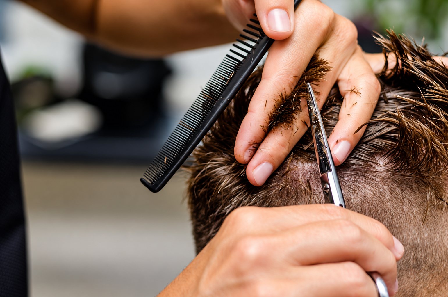 Gros plan sur les mains d’un coiffeur qui coupe les cheveux courts d’un homme avec des ciseaux et un peigne.
