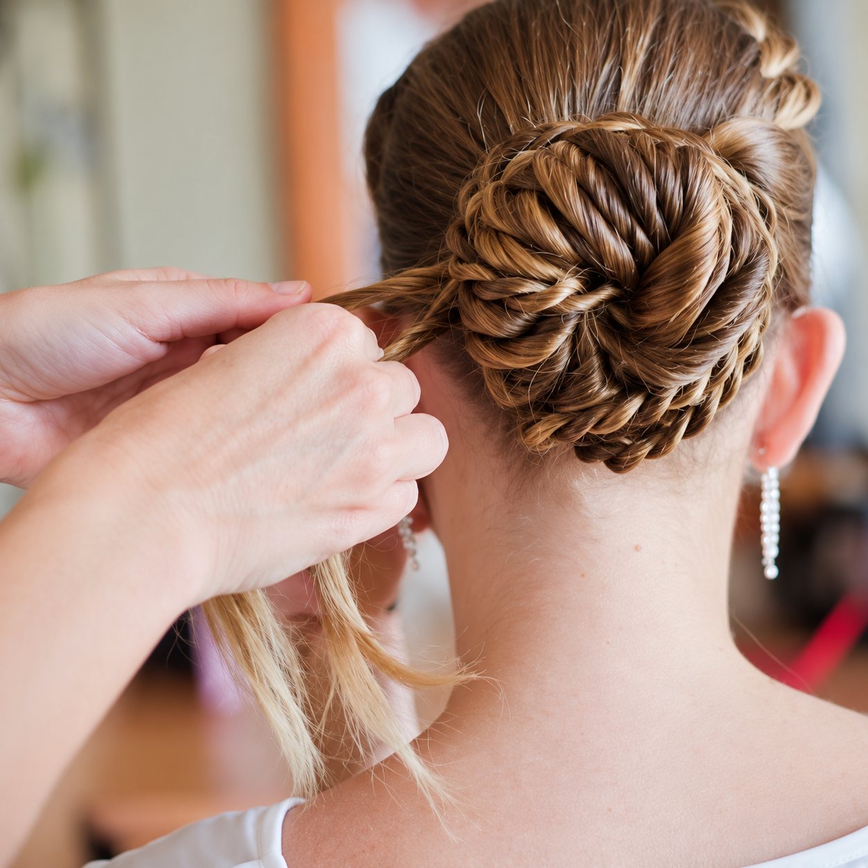Les mains d’une coiffeuse finalisent un chignon torsadé sur la nuque d’une femme portant de longues boucles d’oreilles.